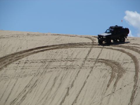 1996 Ford Bronco - A 1996 Ford Bronco navigates a sandy terrain, leaving tire tracks on the dune.