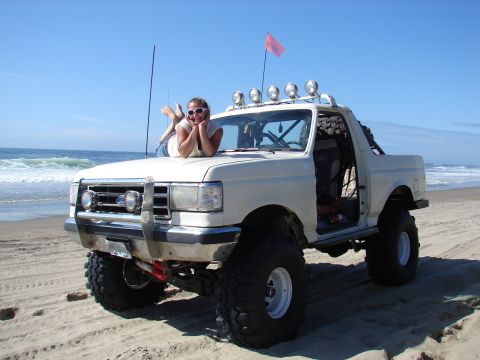 1996 Ford Bronco - A modified white SUV with a woman posing on its hood at the beach.