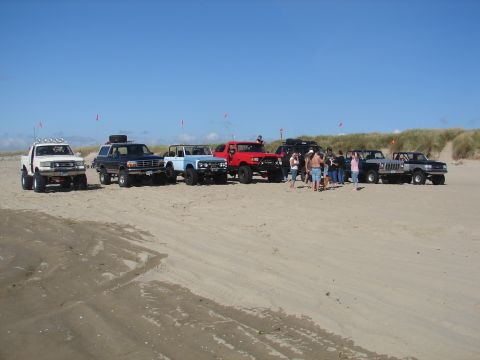 1996 Ford Bronco - Several SUVs, including a 1996 Ford Bronco, are parked on a sandy beach under a clear blue sky.