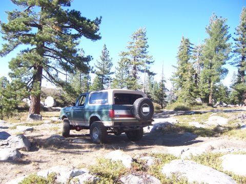 1991 Ford Bronco - This 1991 Ford Bronco is parked off-road amidst rocks and pine trees under a clear blue sky.
