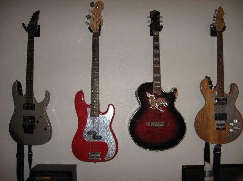 1978 Ford Bronco - Four guitars hang on wall hangers against a plain white wall: a gray superstrat, a red P-bass with a diamond-plate pickguard, a red-burst s…