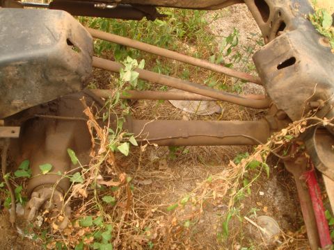 1992 Ford Bronco - The underside of a vehicle is shown, with various metal components and overgrown plants.