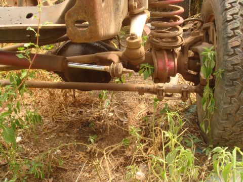 1992 Ford Bronco - Close-up view of the front axle and suspension components, showing rust and vegetation.