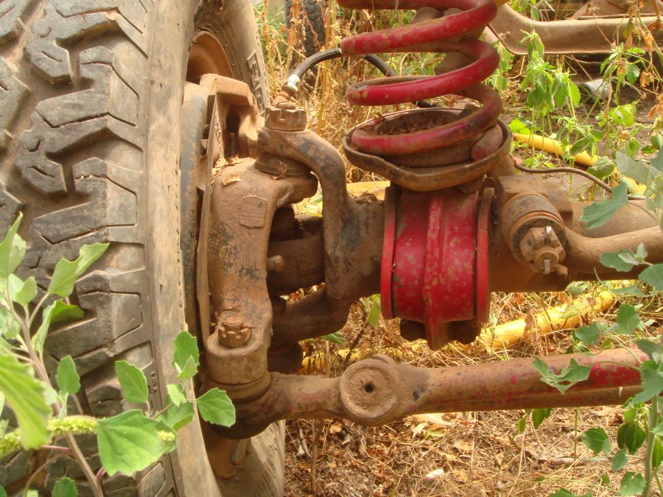 Close-up of a muddy off-road vehicle's front suspension with a red coil spring