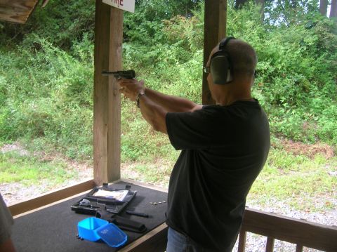 1996 Ford Bronco - A man practices shooting a handgun at an outdoor range, with trees and foliage in the background.