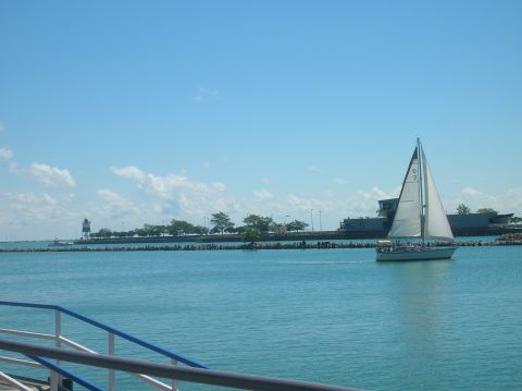 1996 Ford Bronco - A sailboat glides across the water under a clear blue sky, with a distant lighthouse and shoreline.