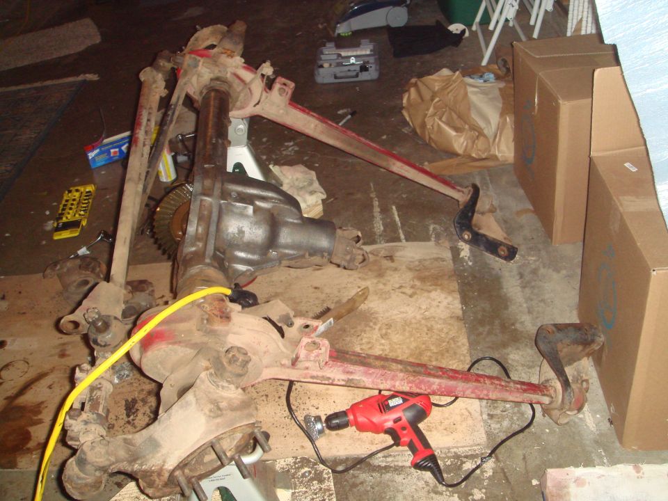 Vehicle axle assembly with differential and suspension components on the floor, with a red drill nearby