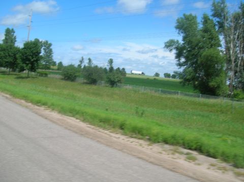 1996 Ford Bronco - A white semi-trailer truck is visible in the distance on a highway, surrounded by green fields and trees under a blue sky.