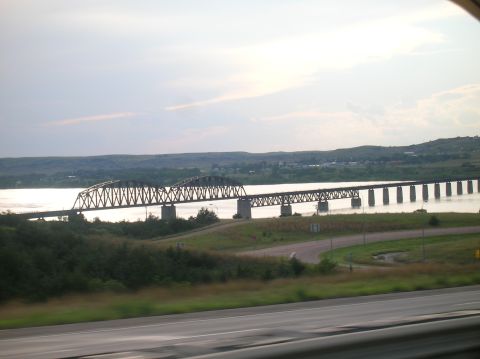 1996 Ford Bronco - A long bridge spans a river, with rolling hills visible on the far bank under a cloudy sky.