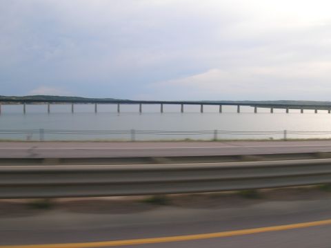 1996 Ford Bronco - A long bridge spans across a calm body of water under a cloudy sky.