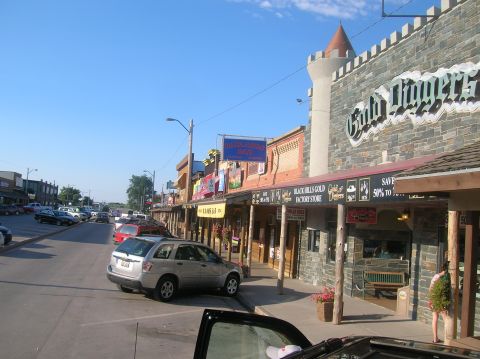 1996 Ford Bronco - A street lined with shops, including 'Gold Diggers', with several cars parked along the curb.