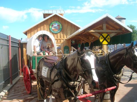 1996 Ford Bronco - A horse-drawn carriage carrying two passengers stops in front of the Wall Drug Railroad building on a sunny day.