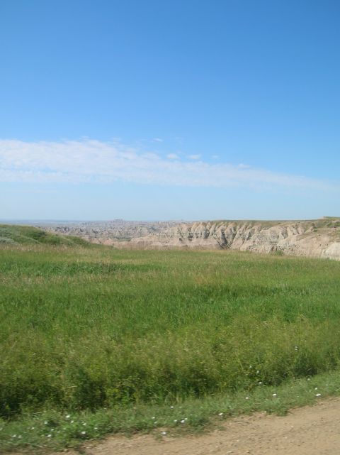 1996 Ford Bronco - A vast landscape of rolling green hills and badlands stretches under a clear blue sky.