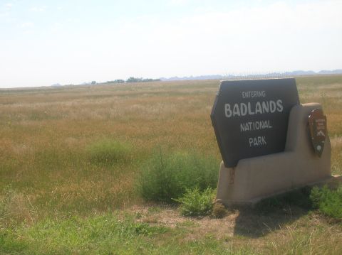 1996 Ford Bronco - Entering Badlands National Park, a sign stands in a wide, open, grassy landscape under a hazy sky.