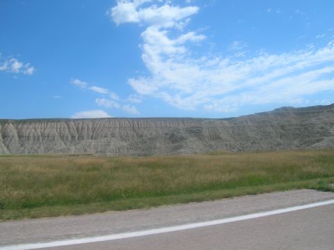 1996 Ford Bronco - A scenic view of eroded hills and a grassy field under a bright blue sky with scattered clouds.