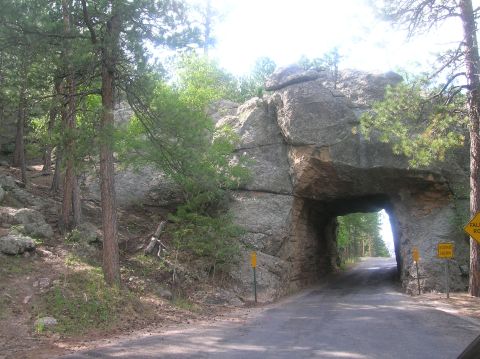 1996 Ford Bronco - A road goes through a natural rock formation tunnel in a wooded area. Yellow signs are posted.