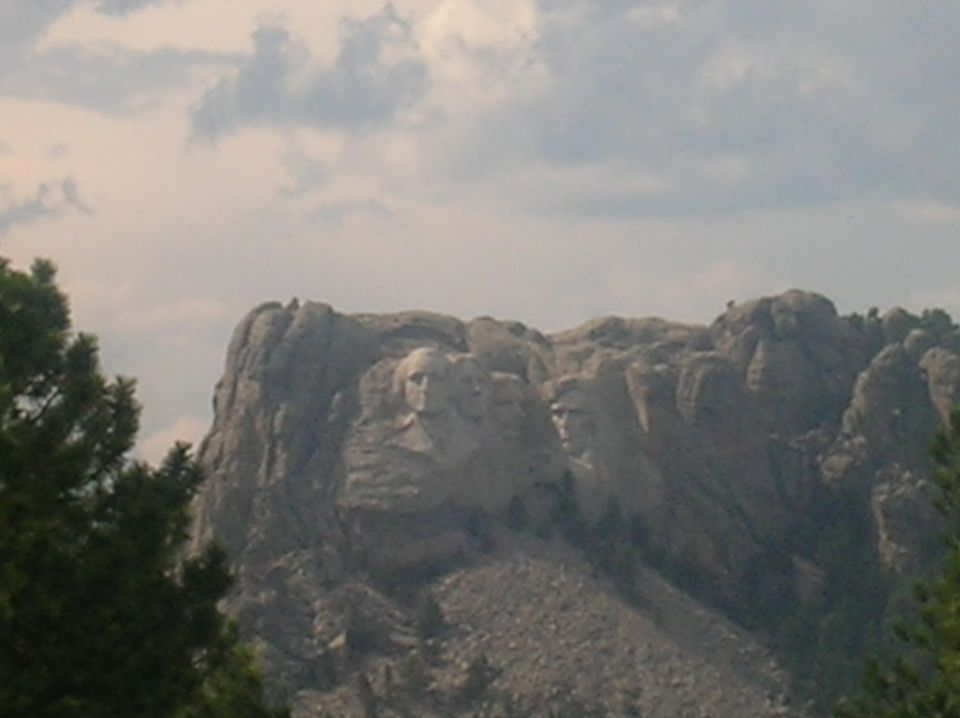 Mount Rushmore National Memorial with presidential faces carved into the rock, viewed from a distance through trees