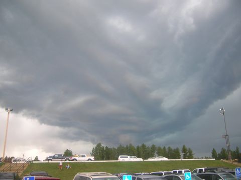 1996 Ford Bronco - A dramatic sky looms over a parking lot filled with vehicles, hinting at an approaching storm.