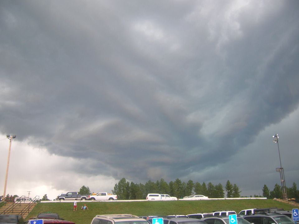 Dark storm clouds gathering over a parking lot with several cars and trucks