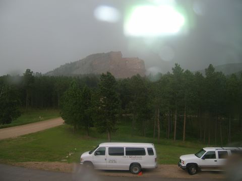 1996 Ford Bronco - Two white vehicles are parked near a dirt road with a forest and mountain in the distance under a cloudy sky.