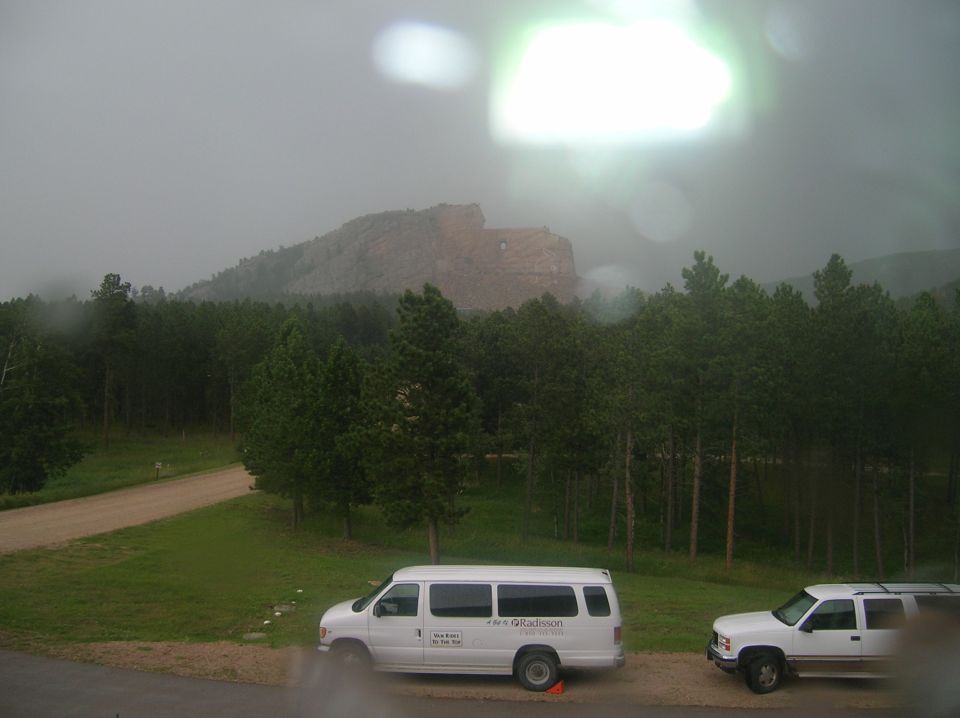 White van and white SUV parked on a wet road with a mountain and forest in the background
