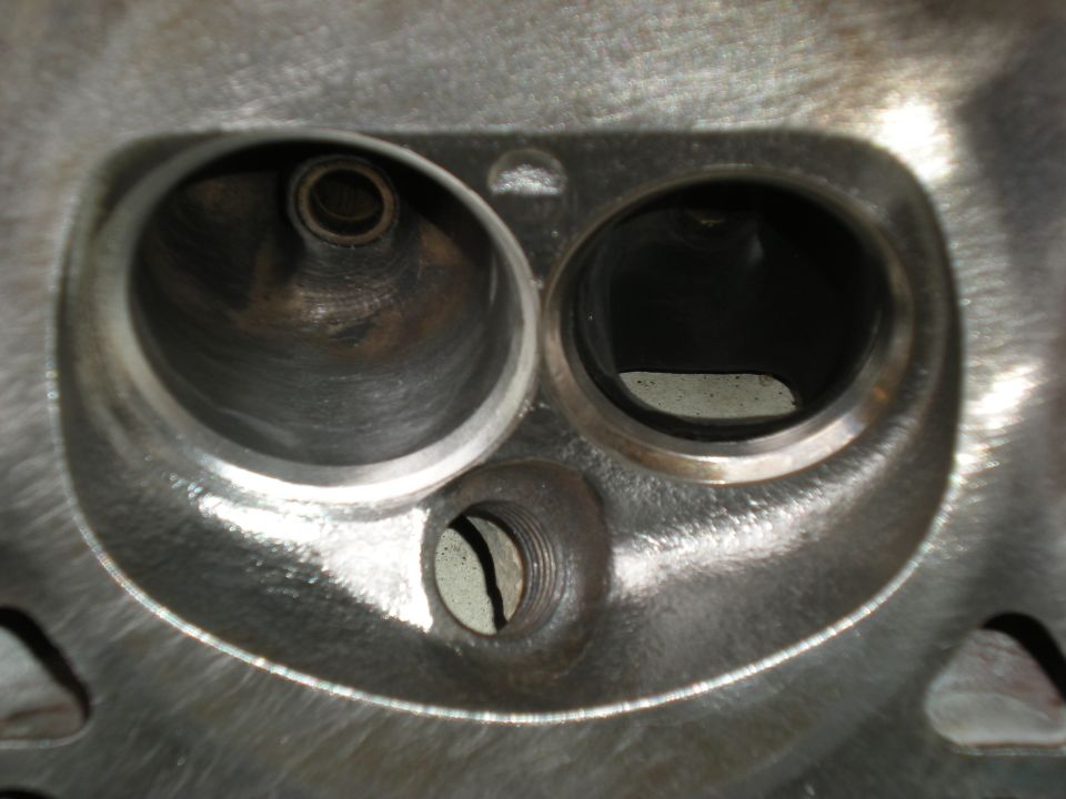 Close-up of an engine cylinder head with two large valve openings and a smaller threaded hole