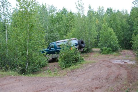 1996 Ford Bronco - A teal Ford Bronco navigates a wooded trail with a spare tire on the rear carrier.