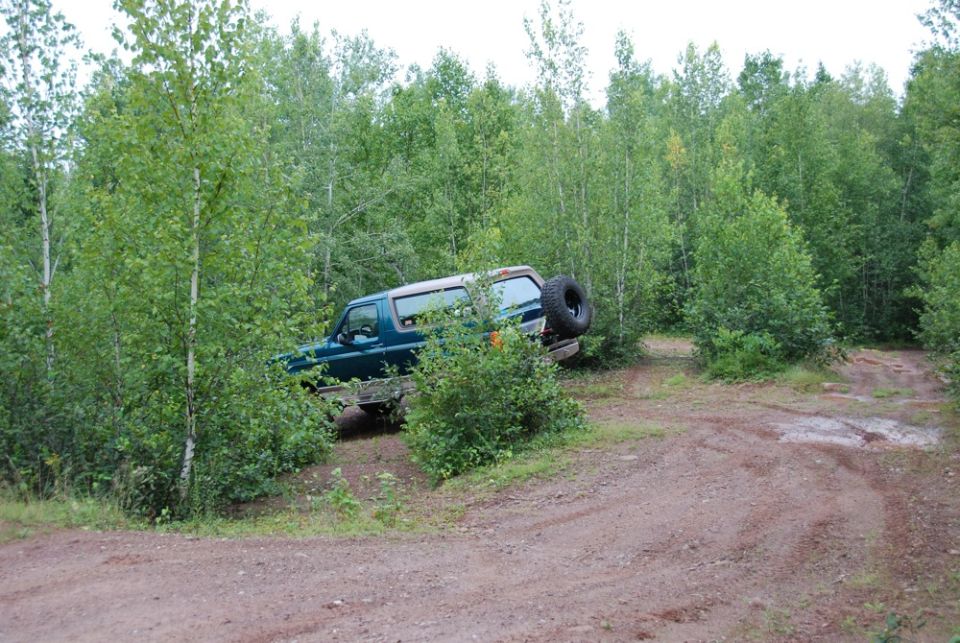 Green Ford Bronco on a dirt path in the woods, spare tire mounted on the back