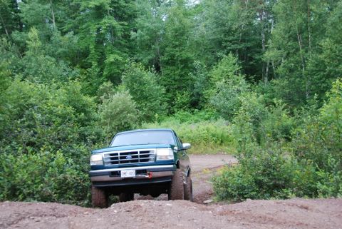 1996 Ford Bronco - A green 1992 Ford Bronco navigates a wooded dirt road, its front grille and bumper clearly visible.