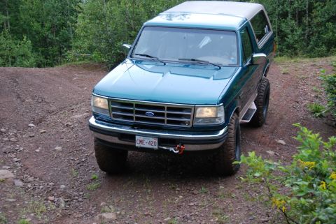 1996 Ford Bronco - Teal Ford Bronco with aftermarket wheels and tow hook on a dirt road.