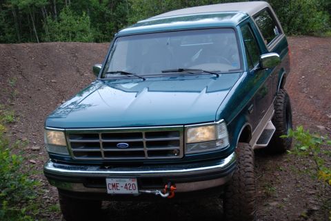 1996 Ford Bronco - A 1996 Ford Bronco is parked on a dirt road surrounded by trees.