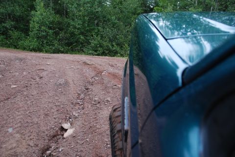 1996 Ford Bronco - SUV driving on a rough dirt road through a wooded area.