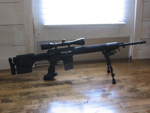 1996 Ford Bronco - A black sniper rifle with a scope and bipod rests on a wooden floor in front of a window.