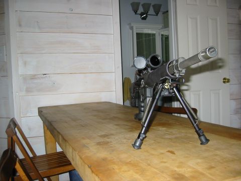 1996 Ford Bronco - A sniper rifle with a bipod is placed on a wooden table indoors.