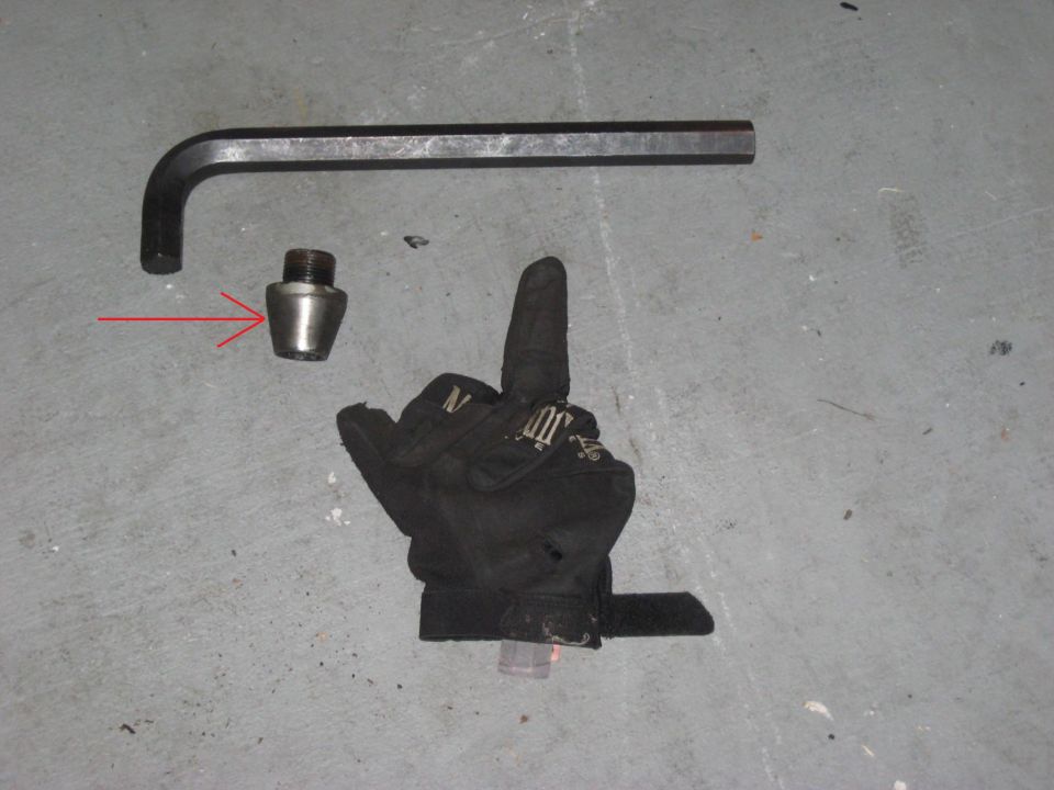 Hex wrench and a lug nut on a concrete floor. Red arrow points to the lug nut