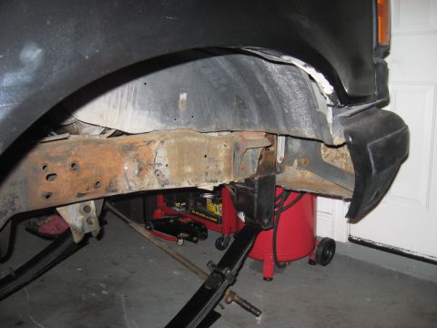 1991 Ford Bronco - Close-up of a vehicle's rusty frame and undercarriage, with a jack supporting it.
