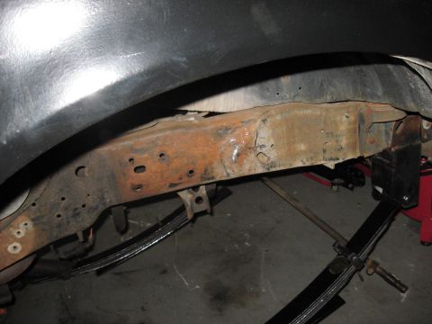 1991 Ford Bronco - Close-up view of the heavily rusted frame and leaf springs beneath a vehicle's fender.