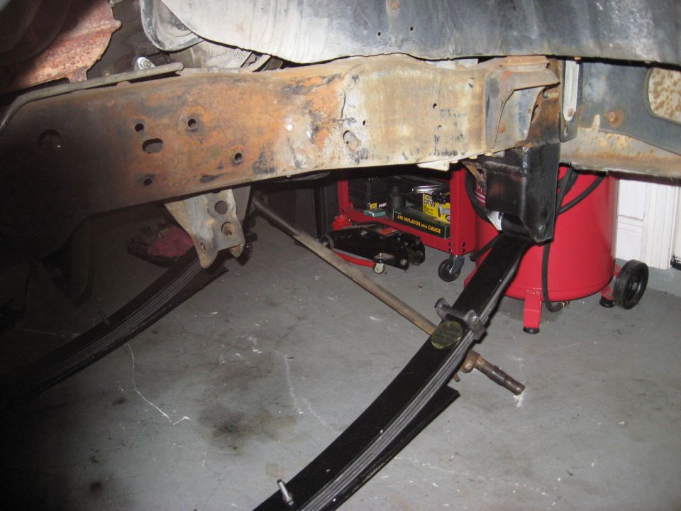 rusted vehicle frame section with leaf springs visible below, air compressor and tool cart in background