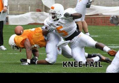2000 Mercury Grand Marquis - A football player in an orange jersey is tackled by an opponent in a white jersey on a grassy field.
