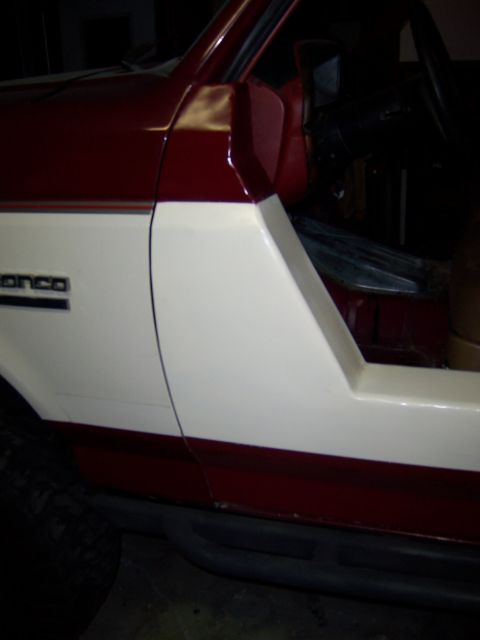 1991 Ford Bronco - Side view of a two-tone red and white Ford Bronco, revealing its door and interior details.