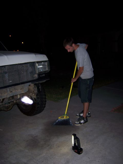 1991 Ford Bronco - A person sweeps the driveway in front of a 1991 Ford Bronco at night.