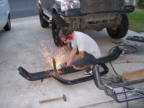 1991 Ford Bronco - A person uses an angle grinder on a metal part near a lifted 1991 Ford F-Series truck.