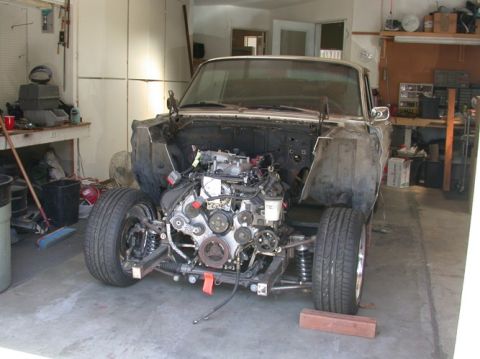 1964 Ford Ranchero - A car sits in a garage with its front end disassembled, revealing the engine bay and suspension components.