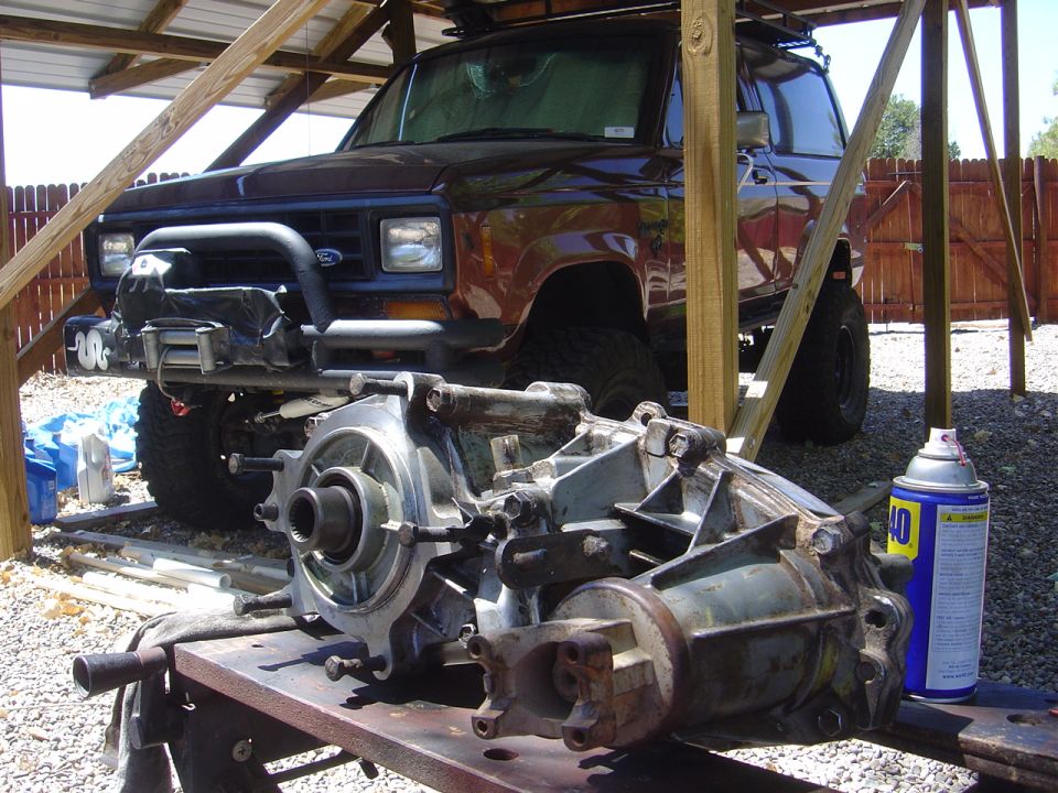 Brown 1986 Ford Bronco II parked under a wooden shelter with transmission parts on a table in front