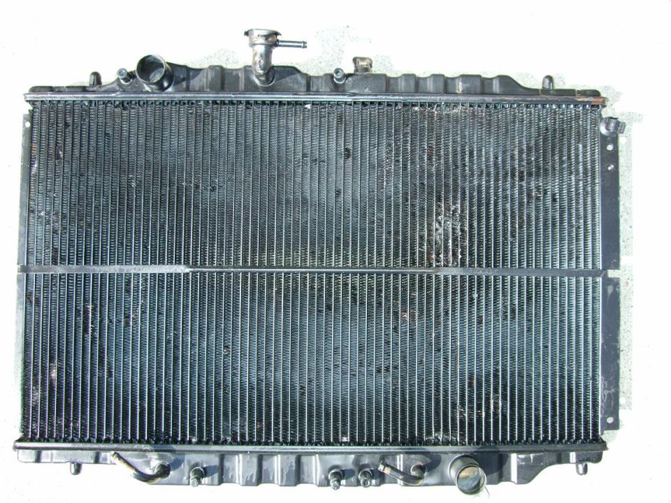Radiator with metal fins and plastic tanks, showing some dirt and debris