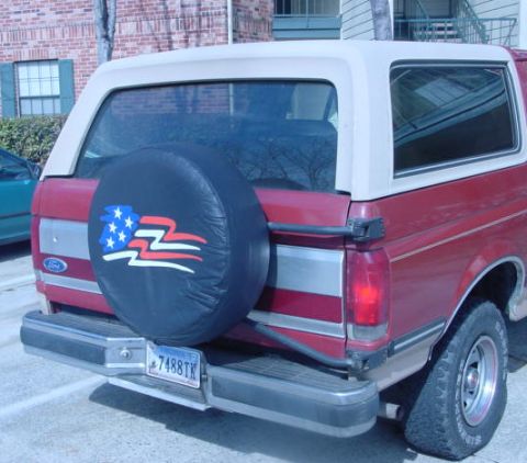 1987 Ford Bronco - The rear of a red 1987 Ford Bronco is visible, a spare tire with an American flag design and a license plate.