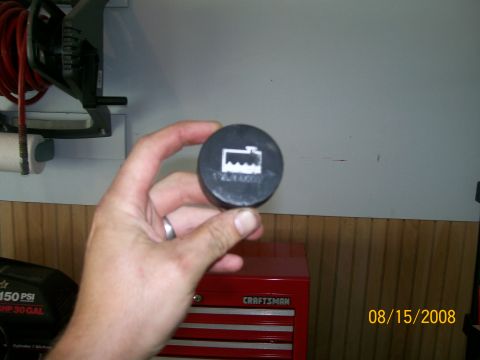 1995 Mercury Grand Marquis - A hand holds a radiator cap displaying a coolant level warning symbol, with a red toolbox and air hose reel in the background.