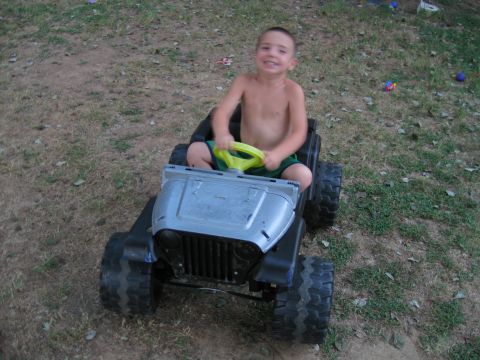 1994 Ford Bronco - A young boy sits in a toy jeep, holding the steering wheel and smiling at the camera.