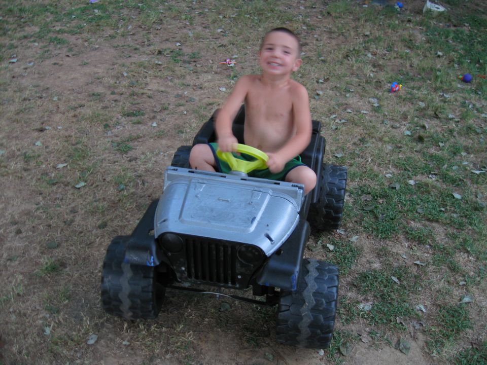 Kid driving a toy jeep with a yellow steering wheel