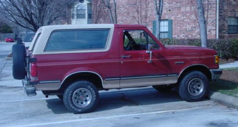 1987 Ford Bronco - This red Ford Bronco is parked in a lot next to a brick building.